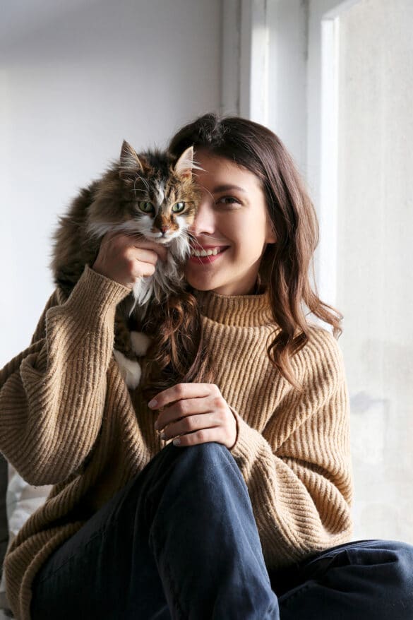 Niedliche Frau hält flauschige Katze an einer Fensterfront, Naturlicht, Wellness, Haustierliebe, Katzenliebhaber, gemütliches Zuhause, Portrait, joy, Tierfreundschaft.